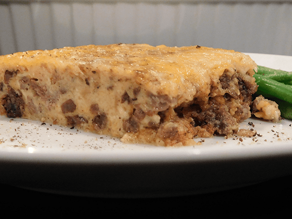 Side view of cooked cheeseburger pie on a white plate with green beans